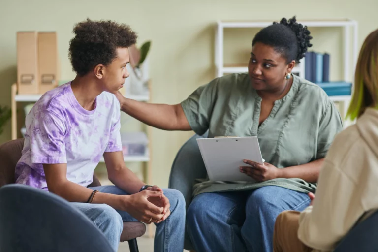 african-young-psychologist-talking-teenage-boy-during-therapy-session-classroom