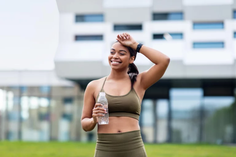 tired-young-black-woman-sportswear-taking-break-during-jogging-wiping-forehead-drinking-water
