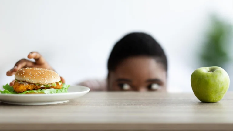 Overweight black woman looking at hamburger from under table selecting between healthy and unhealthy