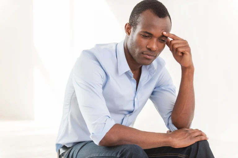 Thinking about... thoughtful young african man in blue shirt touching forehead with hand and looking away