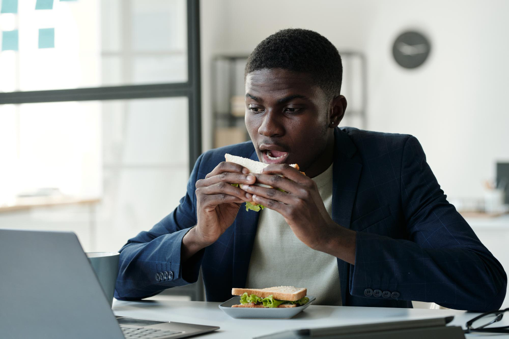 Young hungry office worker in formalwear and eyeglasses eating sandwich