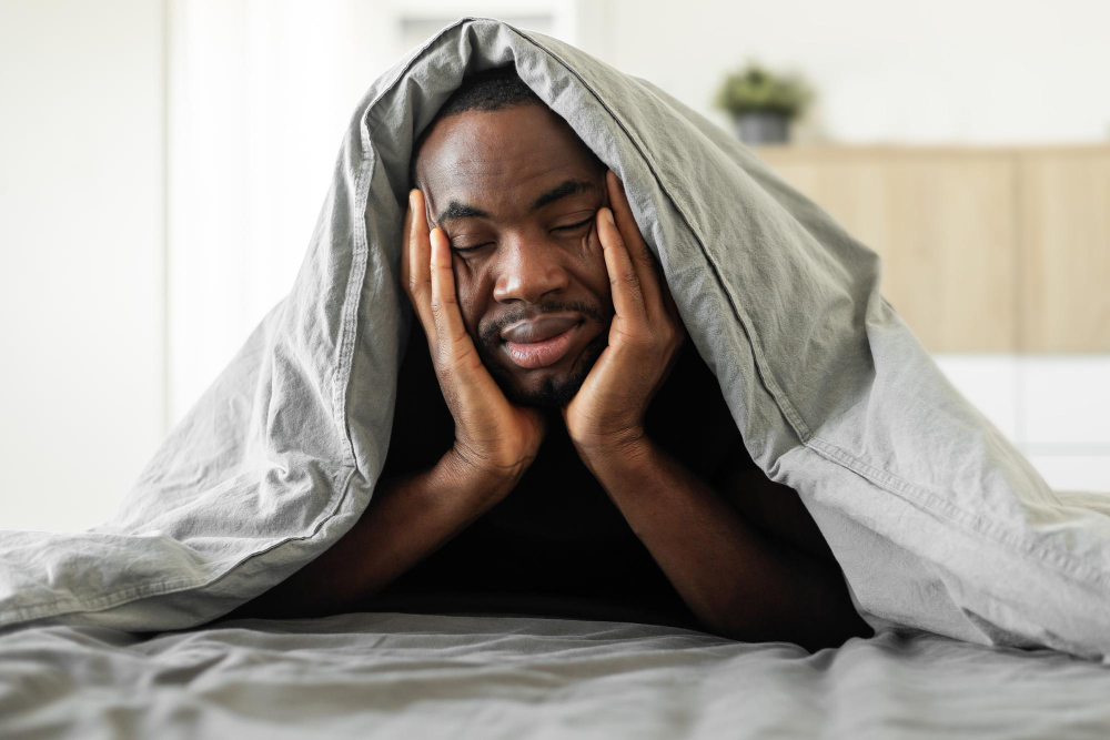 Sleepy African Guy Covered With Blanket Lying In Bedroom