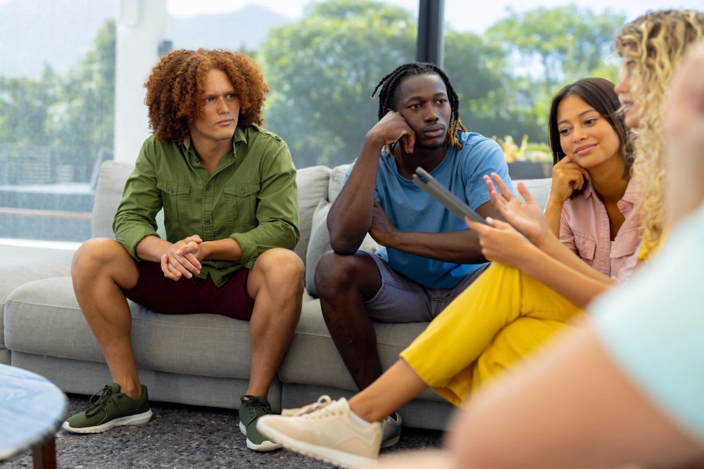 Group of diverse people sitting on sofa, using tablet and talking in group therapy session. Lifestyle, communication, friendship and support, togetherness, unaltered