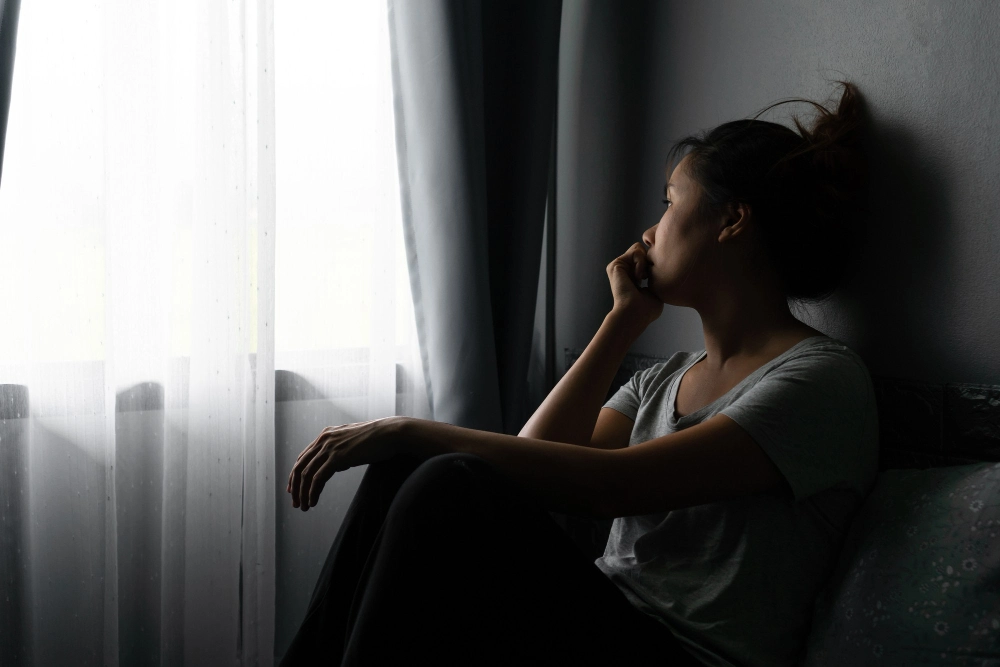 Stressed young Asian woman suffering on depression and sitting alone on bed in dark room at home