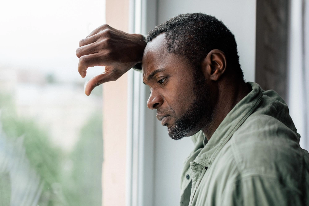 Unhappy frustrated adult african american guy in casual suffering from depression and bad news near window