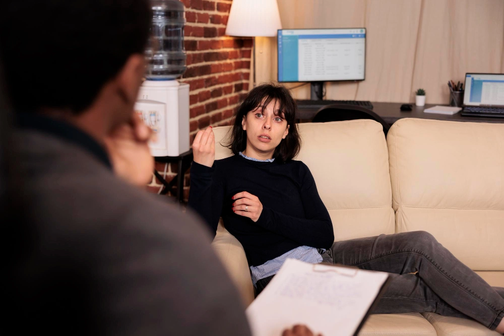 Unhappy woman laying on sofa at psychotherapy session with therapist, talking about stress and problems. Receiving support and help from professional counselor, behavior guidance