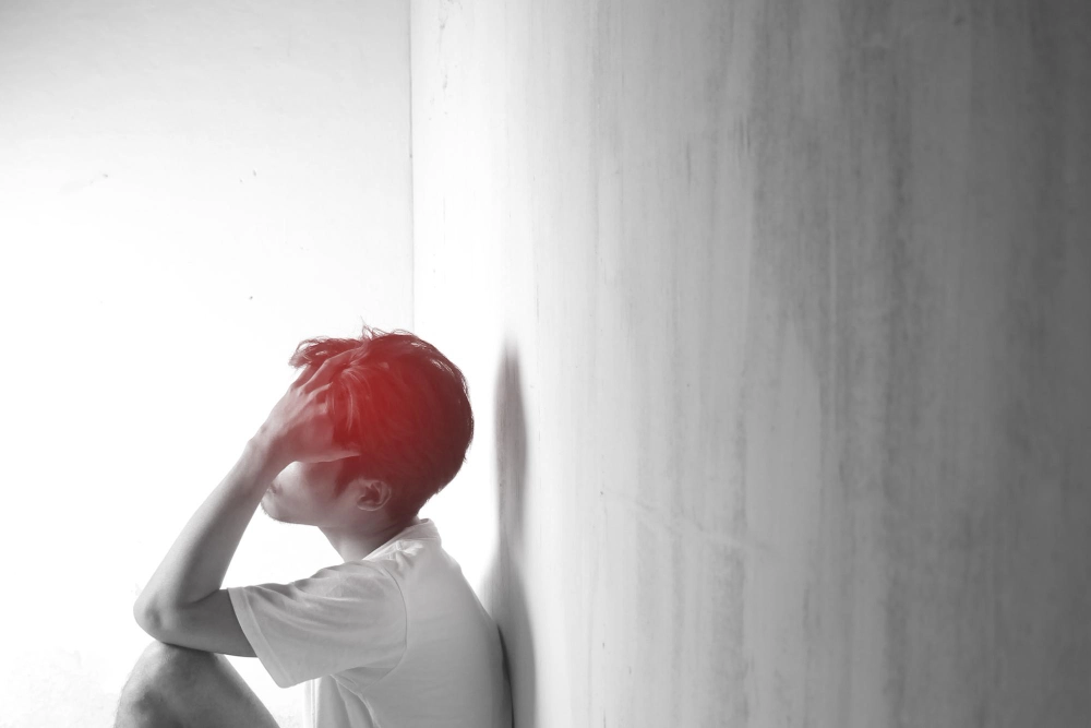 A teenage man with headaches and migraines Man sitting and holding head in indoor room with blurred