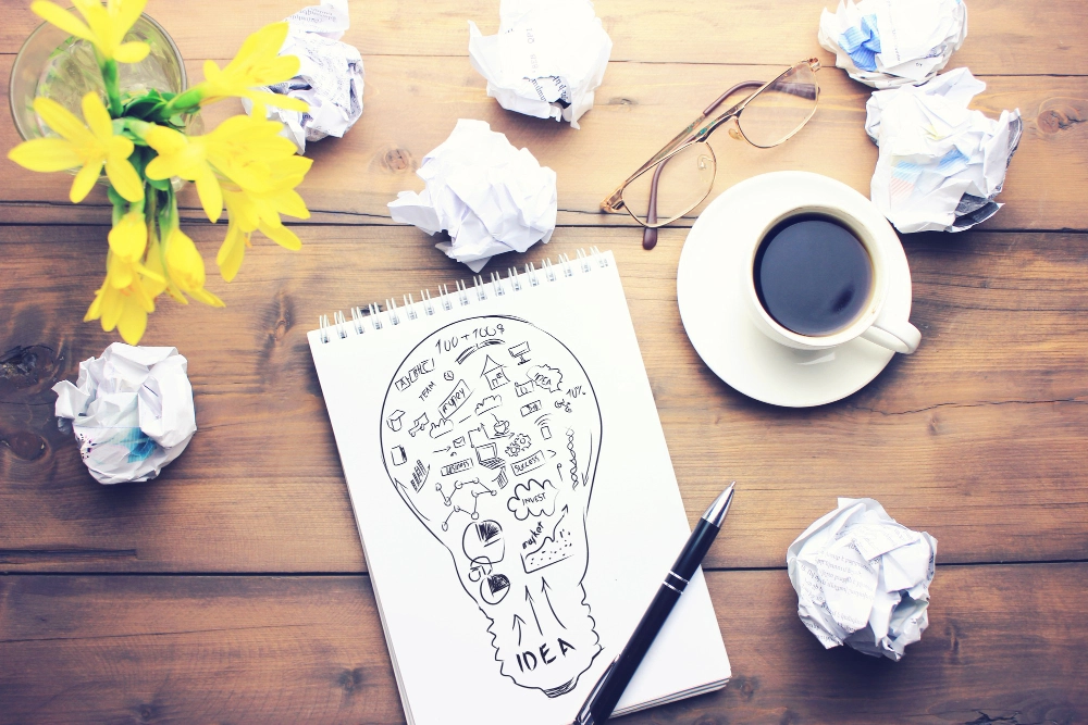 Cup of coffee, pen, notepad, papers, glasses and flower on wooden table